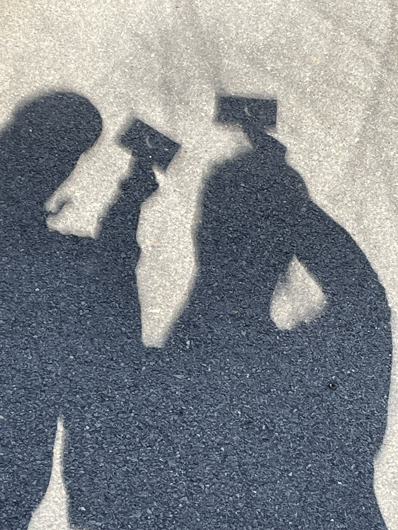 photo of katie and their wife viv's silhouettes during the solar eclipse. they are holding punch cards above their heads to see the eclipe against the pavement.